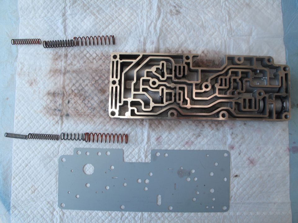 Transmission valve body with intricate channels, next to two sets of springs and a metal plate
