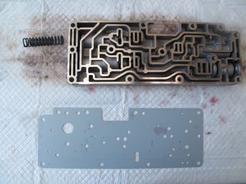 1995 Ford Bronco - Transmission valve body and gasket laid out on a white cloth, with a spring nearby. Text at the bottom reads SUPERMOTORS.