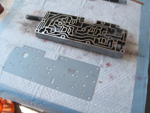 1995 Ford Bronco - Transmission valve body and separator plate disassembled on a white surface. Text on the separator plate is partially visible.