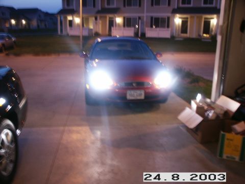 1998 Mercury Sable - A red 1998 Mercury Sable is parked in a driveway at dusk, its headlights illuminated. Another vehicle is partially visible on the left.