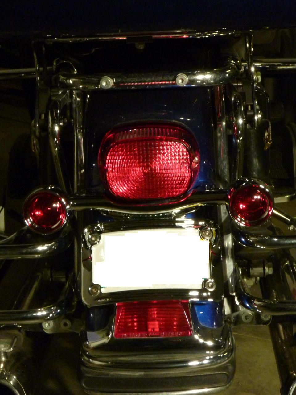 Motorcycle rear with blue bodywork, chrome accents, and a red taillight. Blank license plate area