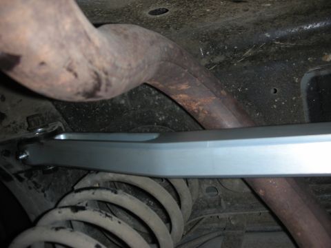 2004 Ford Crown Victoria - Close-up view of the undercarriage, showing an exhaust pipe, a silver bar, and a coil spring.