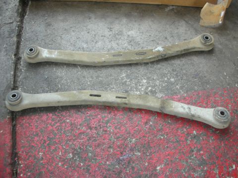 2004 Ford Crown Victoria - Two suspension control arms, likely for a rear axle, are shown laid out on a workshop floor.