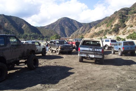 1995 Ford Bronco - A group of off-road vehicles, including a 1995 Ford Bronco, are gathered in a dusty area with mountains visible in the background.