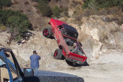 1995 Ford Bronco - This red off-road vehicle is navigating a challenging rocky terrain, with another vehicle partially visible in the foreground.
