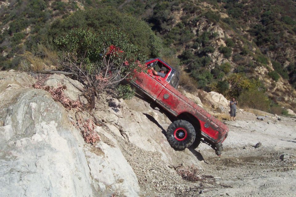 Red off-road truck tilted on a rocky incline, driver visible inside
