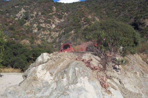 1995 Ford Bronco - A red 1995 Ford Bronco is seen partially obscured by trees and rocks on a steep, off-road incline.