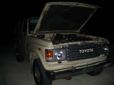 1986 Toyota Land Cruiser - The front of a beige Toyota Land Cruiser is visible with its hood open, revealing the engine compartment.