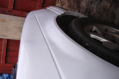 1990 Ford Taurus - Close-up view of the side of a white 1990 Ford Taurus, showing the fender and wheel.
