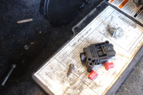 1990 Ford Taurus - Ford Motor Company catalog part box holding a black electrical sensor, oil drain plug, and red plastic caps.
