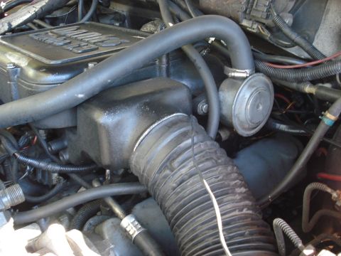 1992 Ford C-350 (Centurion Conversions) - Tight engine-bay view of a black plastic intake elbow and accordion air duct clamped to an airbox, with a large rubber crankcase hose arcin…