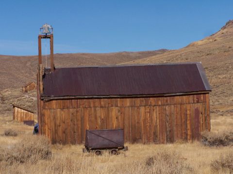 1990 Ford Bronco - Old wooden structures and a mine cart sit in a dry, grassy landscape under a clear blue sky.