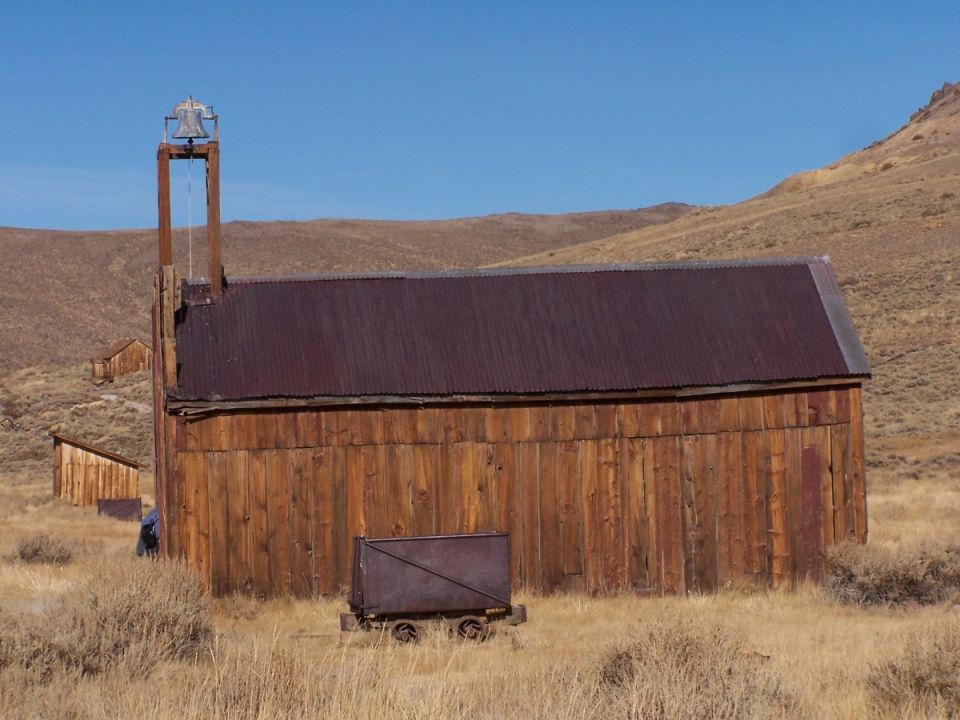 Abandoned mine cart in front of weathered wooden buildings with a bell tower