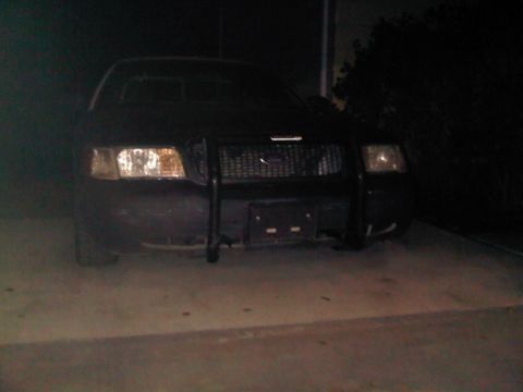 2003 Ford Crown Victoria - A black Ford Crown Victoria Police Interceptor is parked on a concrete surface at night, its headlights illuminated.
