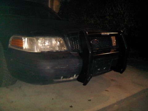 2003 Ford Crown Victoria - The front of a black 2003 Ford Crown Victoria is visible, equipped with a heavy-duty push bar.