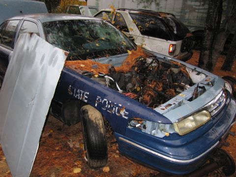 1991 Ford LTD Crown Victoria - A blue 1991 Ford Crown Victoria LTD police car sits in a junkyard with its hood open, revealing the engine compartment.
