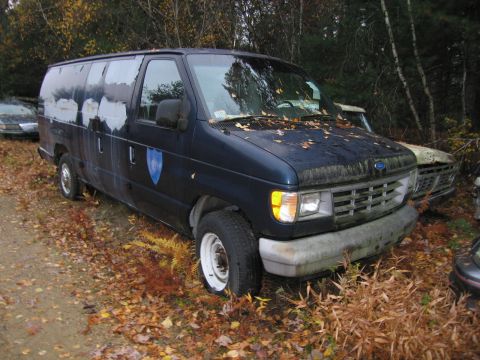 1991 Ford LTD Crown Victoria - A dark blue van sits in a junkyard with other vehicles and fallen leaves.