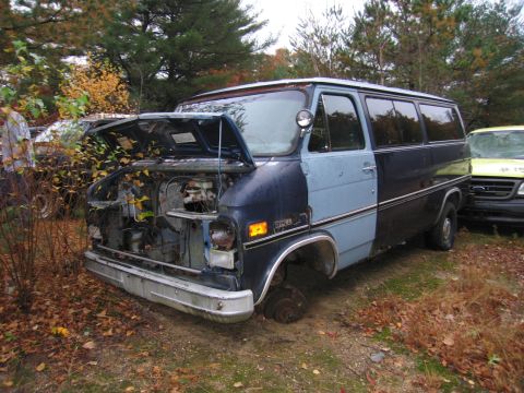 1991 Ford LTD Crown Victoria - Abandoned van sits in a yard, missing a wheel and with its hood up, next to another vehicle.