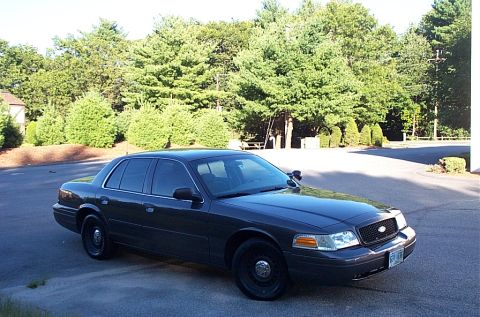 2001 Ford Crown Victoria - This dark sedan, identified as a 2001 Ford Crown Victoria, is parked outdoors on a sunny day.