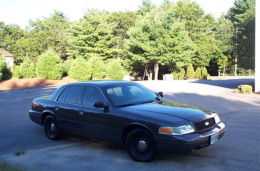 Dark sedan parked on asphalt with trees in background. License plate is visible