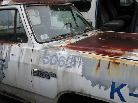 1991 Ford LTD Crown Victoria - Side view of a heavily rusted white pickup truck with "POWER RAM" badging and blue numbers.