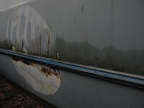 1991 Ford LTD Crown Victoria - Close-up of a damaged car door panel showing rust and a partially removed sticker.