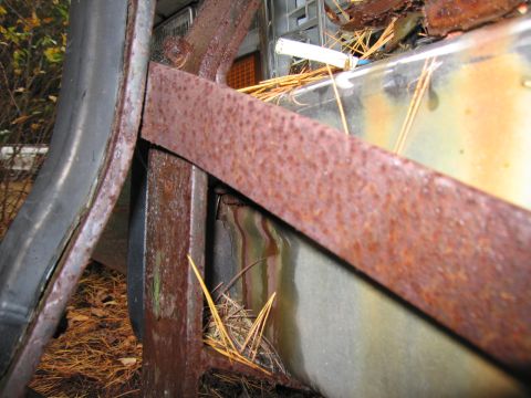 1991 Ford LTD Crown Victoria - Close-up view of heavily rusted metal components and a tire, suggesting a derelict vehicle.