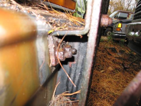 1991 Ford LTD Crown Victoria - A close-up view of a rusted metal bracket and bolt, with pine needles scattered around.