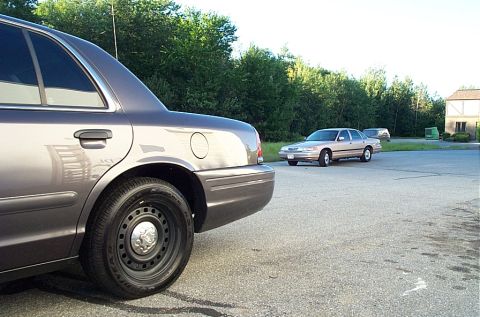 2001 Ford Crown Victoria - A gray sedan is parked in the foreground, with a tan sedan visible in the background of the lot.