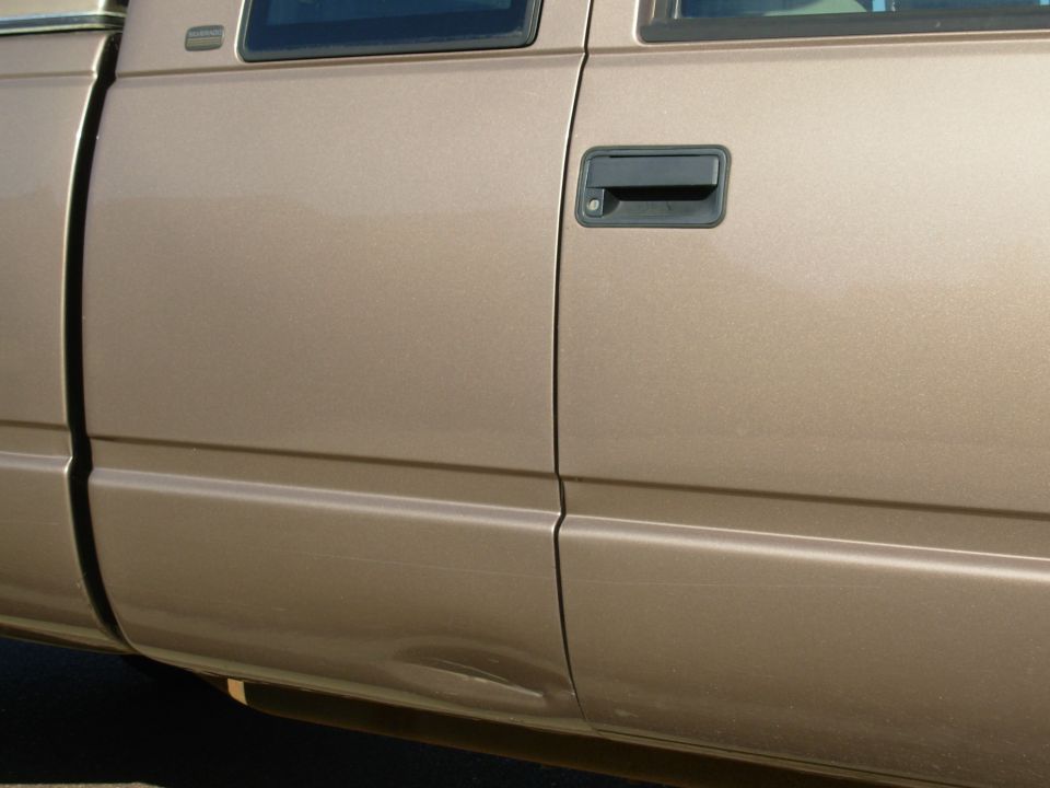 Close-up of gold pickup passenger door with black handle and shallow dent near the rocker