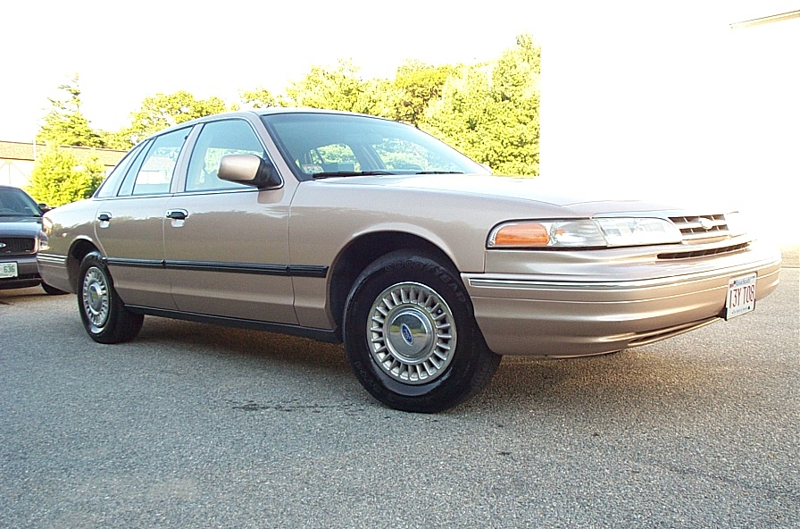 Tan 2001 Ford Crown Victoria, front 3/4 view, parked on asphalt, with another vehicle to the left