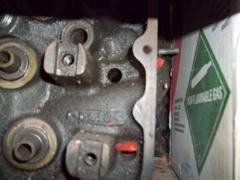 Bare cast-iron cylinder head deck with rocker pedestals beside a green non-flammable gas cylinder