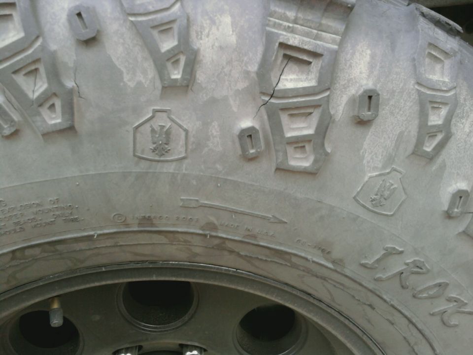 Close-up of a tire tread with a crack and some embossed symbols. Text on the tire is visible