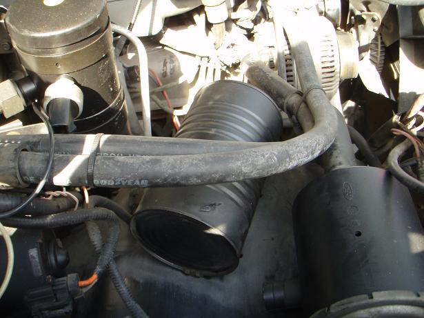 Engine bay showing a large black air intake hose and other engine components. Text 'GOODYEAR' is visible on a hose