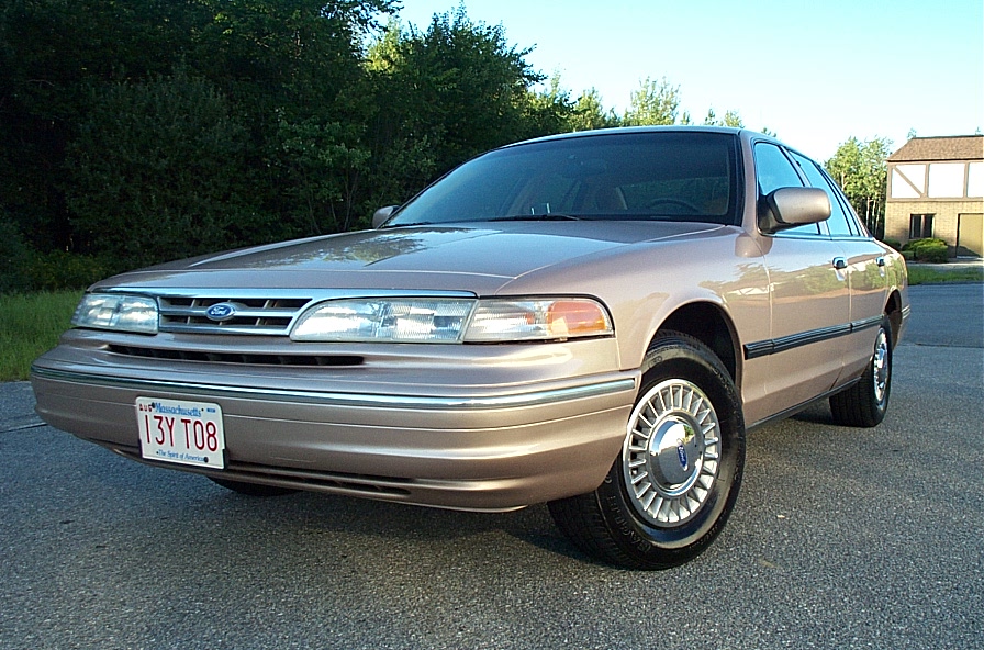 Tan 2001 Ford Crown Victoria parked on asphalt with trees and a house in the background