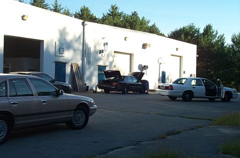 2001 Ford Crown Victoria - Several Ford Crown Victorias are parked in front of a commercial building, with two of them having their hoods open.