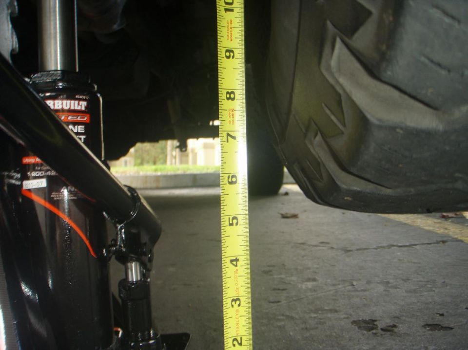 Measuring ground clearance next to a tire with a tape measure and a jack