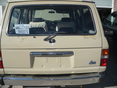 1986 Toyota Land Cruiser - This beige SUV features a 4WD badge on the rear and shows signs of rust around the tailgate.