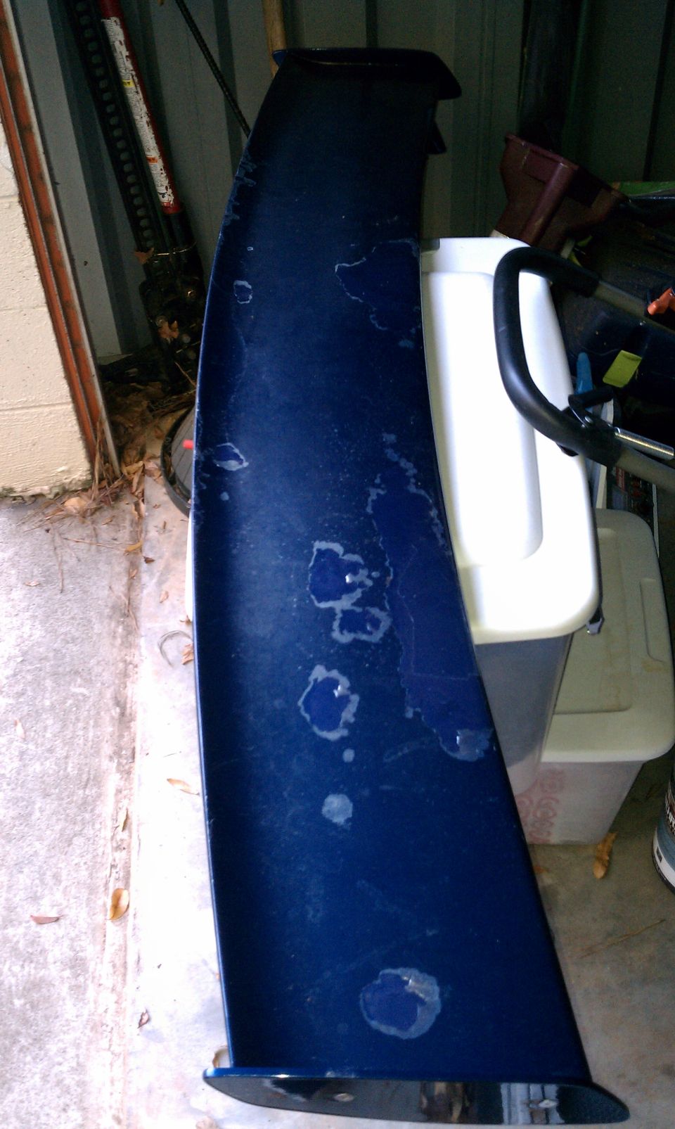Blue car spoiler with peeling paint and water spots
