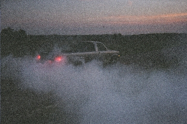 1988 Ford LTD Crown Victoria - Grainy dusk photo of a light-colored pickup truck doing a burnout on a rural road, its glowing red taillights cutting through a heavy cloud…