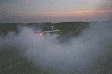 1988 Ford LTD Crown Victoria - Dusk shot of a car nearly buried in a thick bank of white tire smoke on a rural road, with only its roofline and a single glowing red taill…