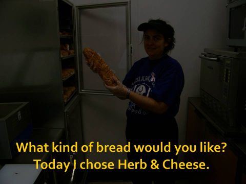 1989 Ford Bronco - A person holds a loaf of herb and cheese bread in a commercial kitchen, with racks of bread visible in the background.