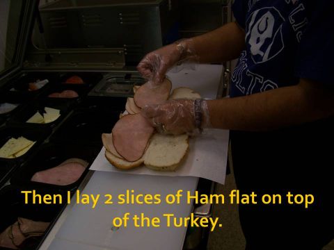 1989 Ford Bronco - A person is shown making a sandwich, layering ham on bread at a sandwich counter.