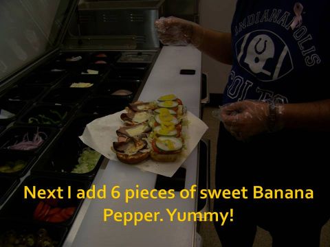 1989 Ford Bronco - A person is adding banana peppers to a sandwich at a food preparation station.