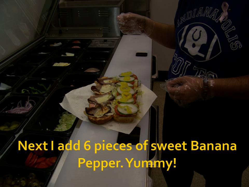 Sandwich being made with banana peppers and other toppings