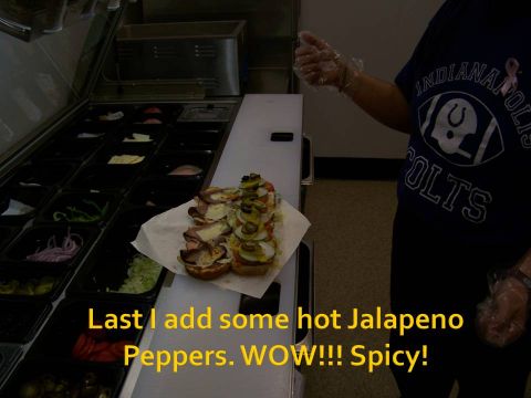 1989 Ford Bronco - A sandwich is being prepared with various toppings, including jalapenos, at a food service counter.