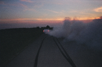 1988 Ford LTD Crown Victoria - Dusk burnout shot taken from behind a car on an open road, with twin black tire stripes laid down on the pavement and a thick cloud of whit…