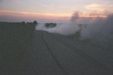 1988 Ford LTD Crown Victoria - Twin dark tire stripes laid down on a dark rural road at dusk, disappearing into a cloud of white tire smoke that drifts across the field t…