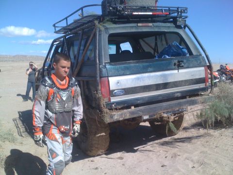 1989 Ford Bronco - A modified Ford Bronco sits in a desert landscape with a person in motocross gear nearby.