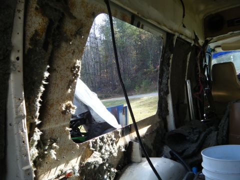 1981 Ford E350 - The interior of the van shows significant damage and missing insulation, with a view of the outdoors through a large opening.